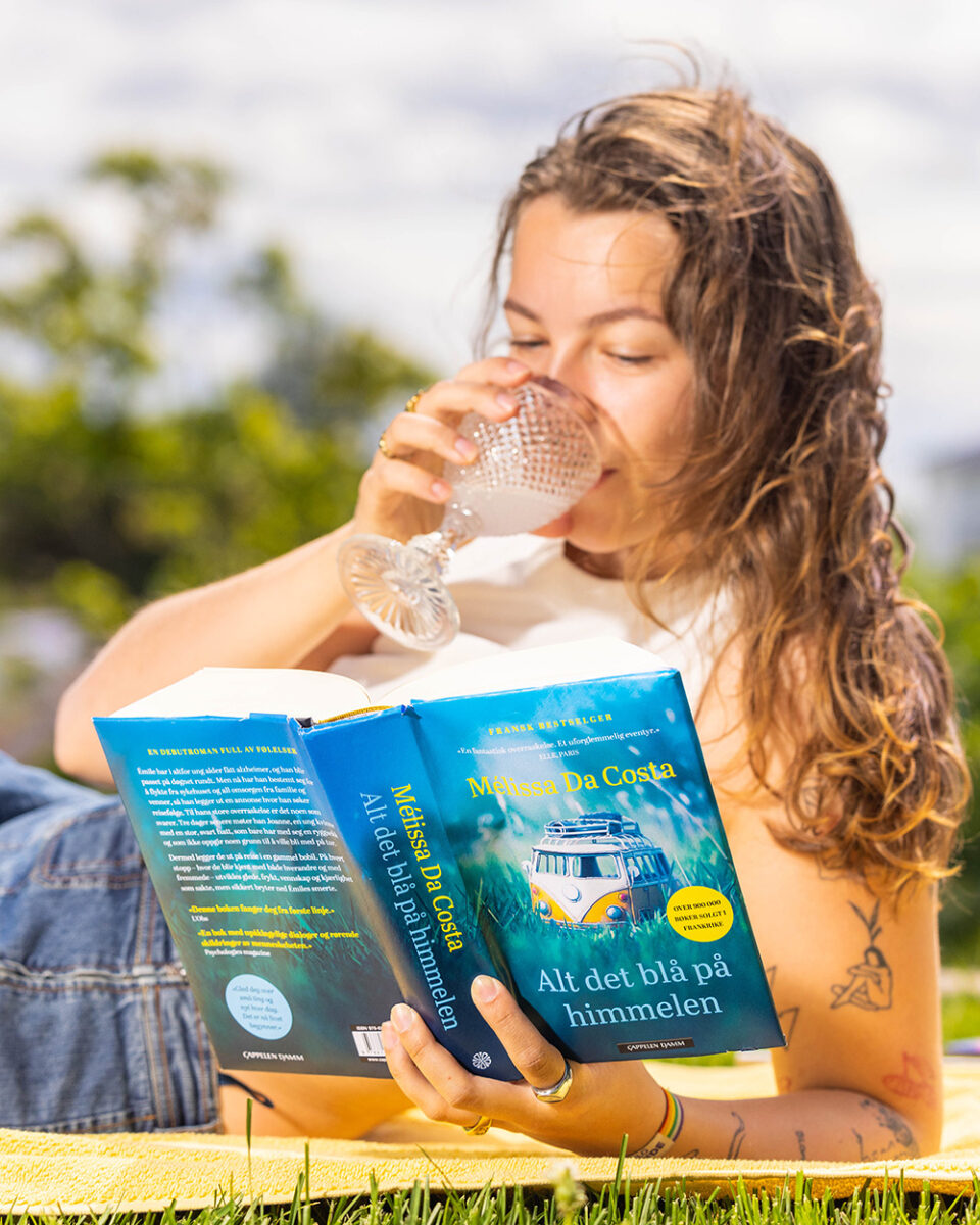 Foto av jente som ligger i en park og leser Mélissa Da Costas bok "Alt det blå på himmelen".