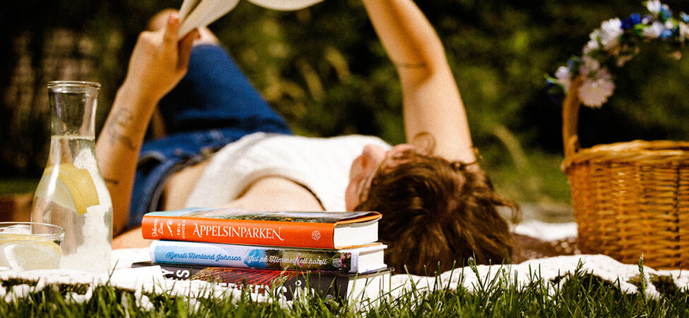 Foto av jente som leser på gresset, sommerens beste bøker 2024